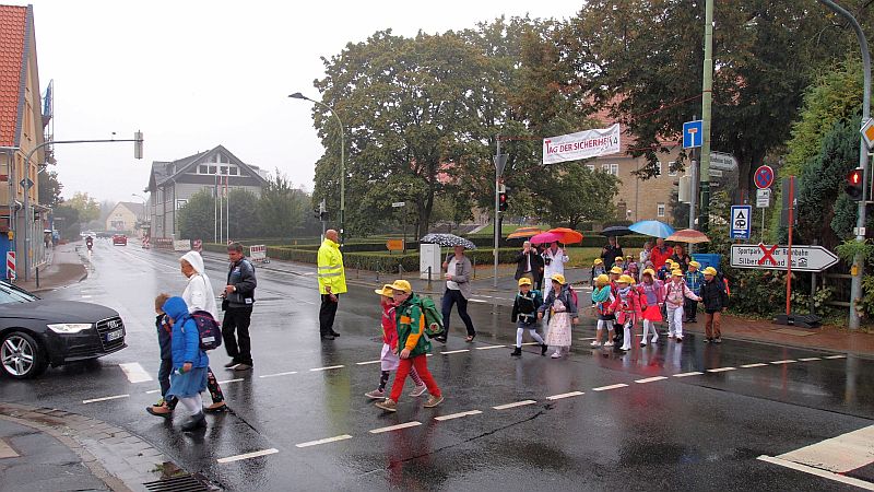Die Schülerinnen und Schüler der Klasse 1a werden von ihrer Klassenlehrerin Frau Scheltens bei Nieselregen über die Straße geführt