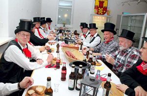 In traditioneller Bekleidung - weißes Hemd, rotes Halstuch, schwarzer Zylinder wurde Mettwurst gegessen